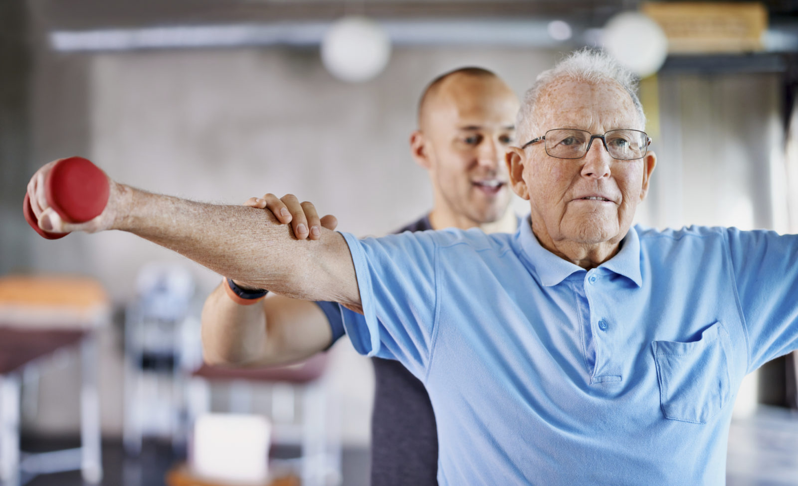 Physical therapist helping a senior man with weights