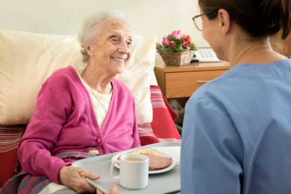 caregiver helping elderly woman at mealtime