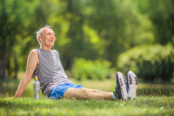 Active senior man in sportswear sitting in park and listening to music on headphones