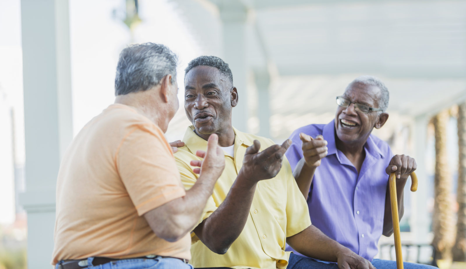 Three senior men sitting on a porch, talking, smiling and laughing