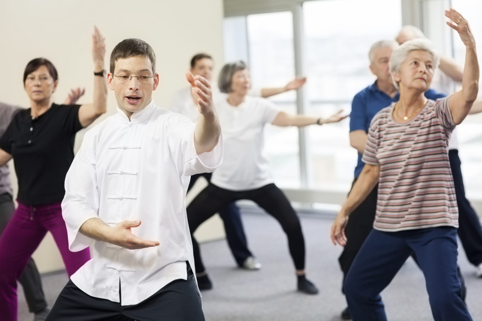 Group of senior adults practicing tai chi with an instructor in the community center.
