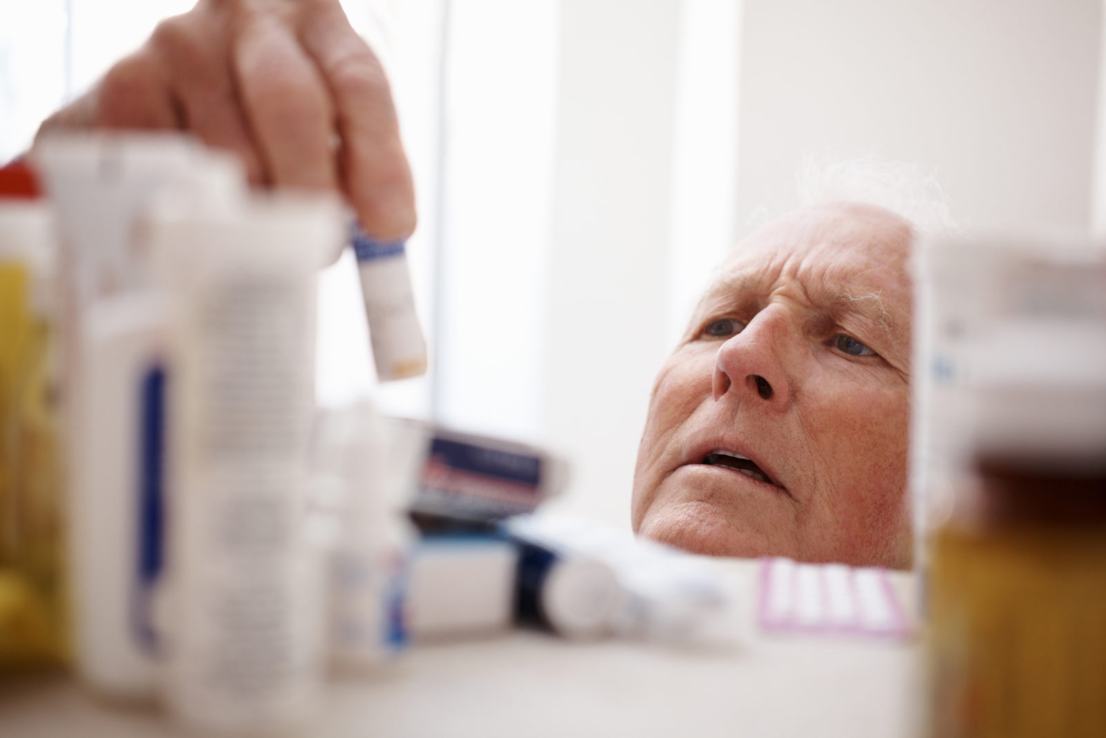 Elderly man searching for correct medication in medicine cabinet