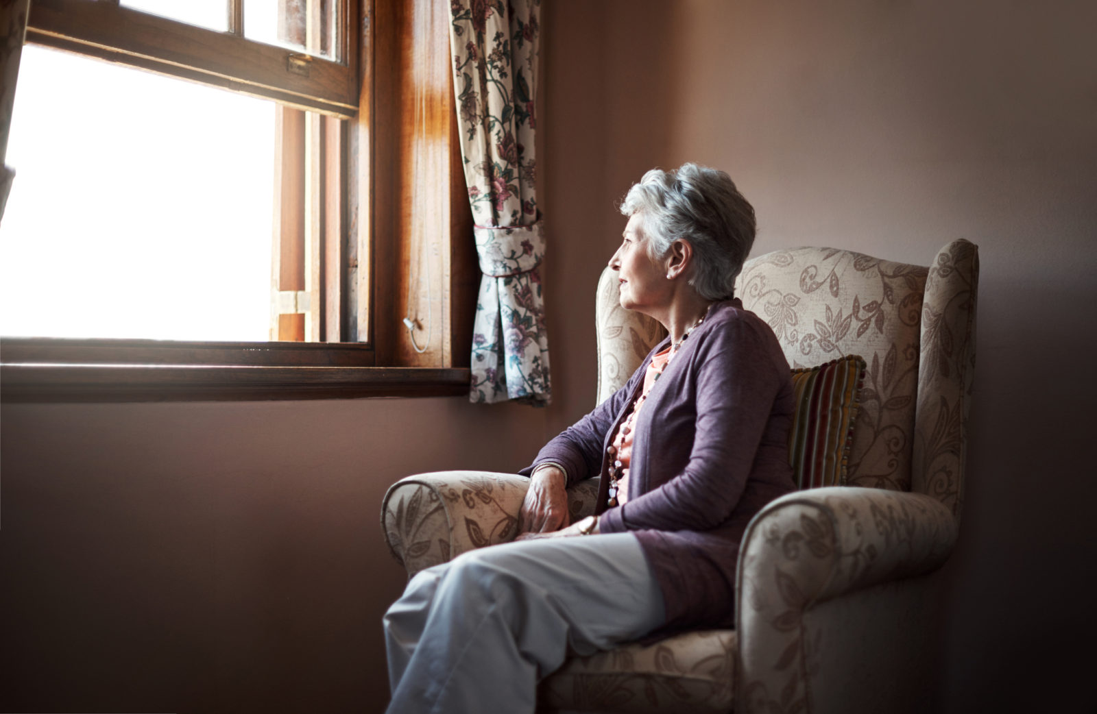 Senior woman sitting in living room in front of window, starting outside