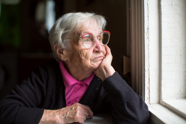 Elderly woman in glasses staring out the window.