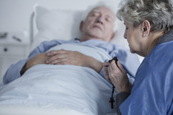 Elderly woman praying with rosary for the health of sick husband