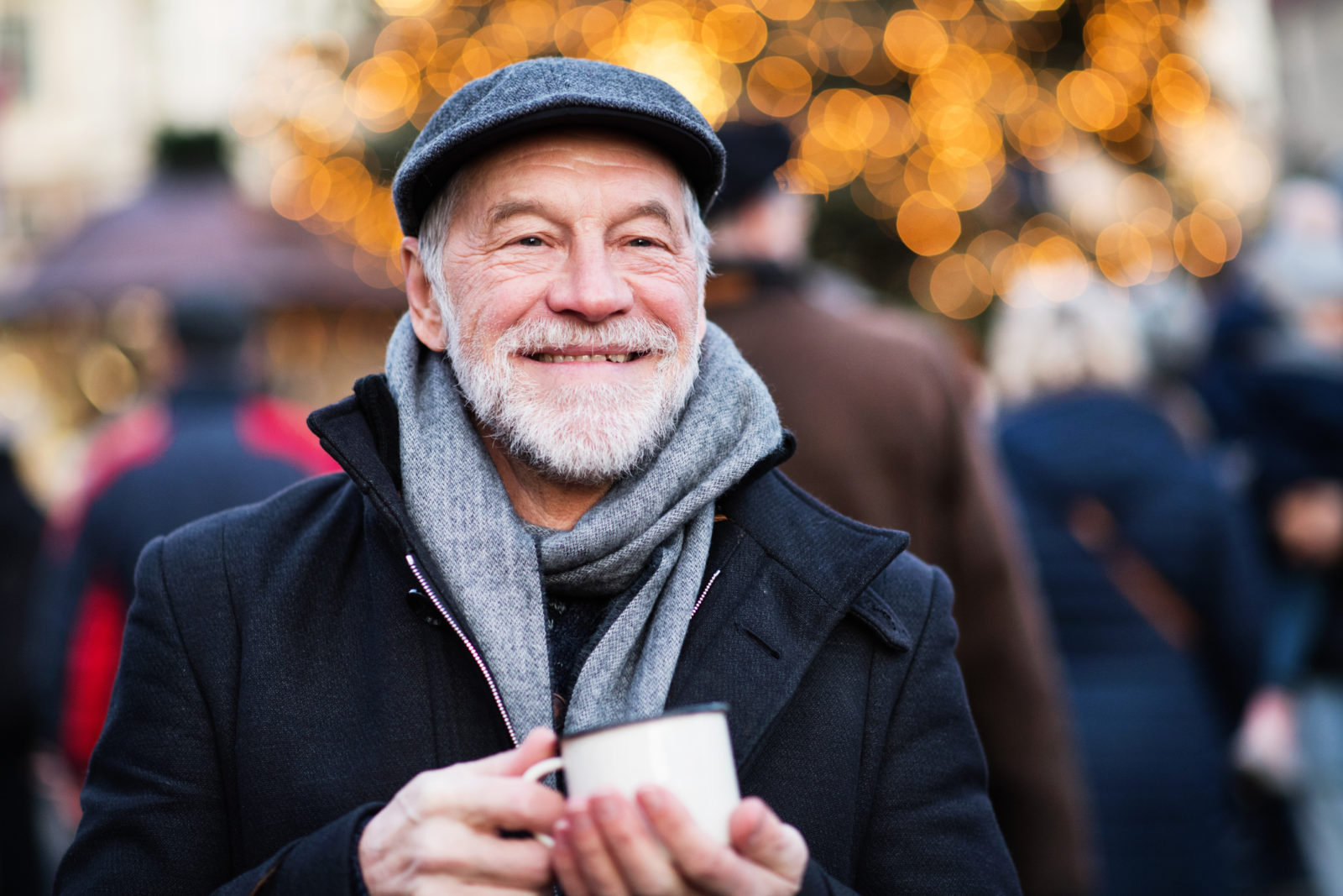 Happy senior man on an outdoor Christmas market, holding enameled cup in winter time.